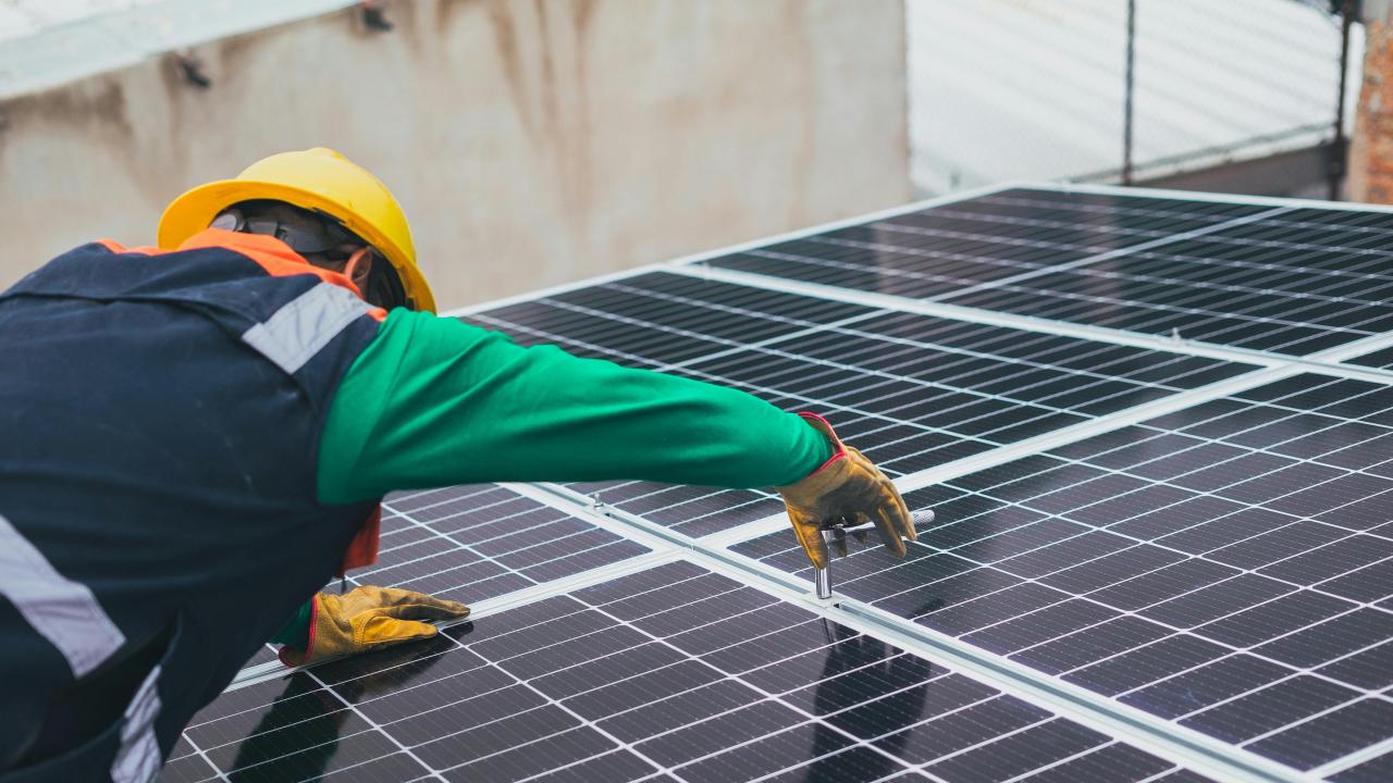 Un uomo con casco e occhiali protettivi lavora su un pannello solare.